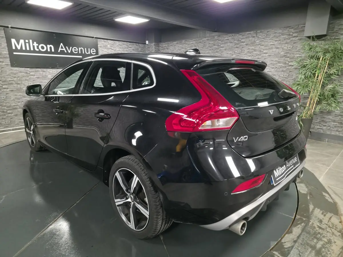 Vue 3/4 arrière droite d'une Volvo V40 D2 R-Design noire avec jantes alliage IXION et double sortie d'échappement chromée.