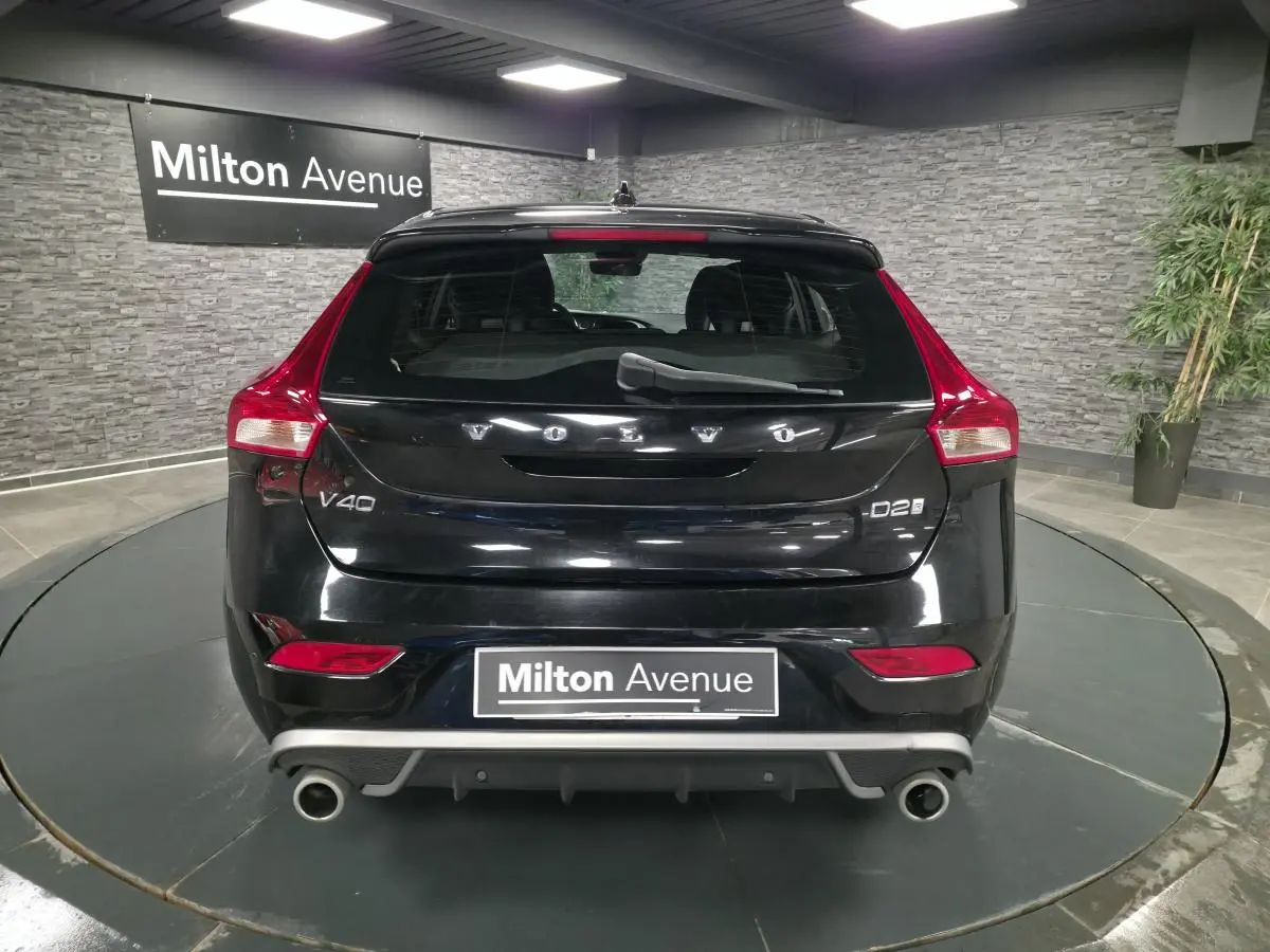 Vue arrière d'une Volvo V40 D2 noire avec double sortie d'échappement et feux arrière LED dans un showroom.
