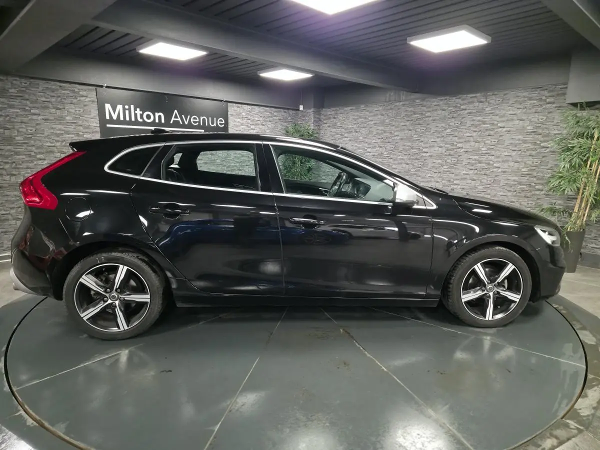 Profil côté gauche d'une Volvo V40 D2 R-Design noire avec jantes alliage Ixion 17 pouces dans un showroom.