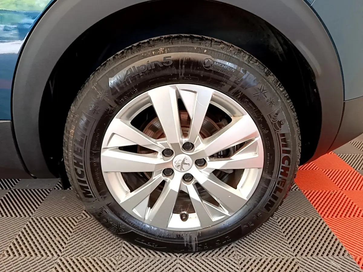 Gros plan sur la roue avant droite d’un Peugeot 3008 bleu, jante alliage argentée avec logo lion au centre.