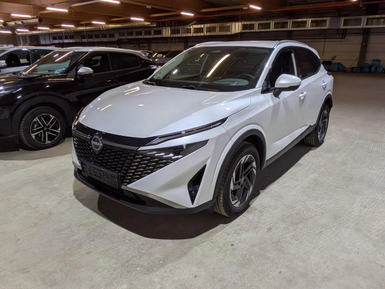 Nissan Qashqai blanc nacré vu en 3/4 avant droit dans un parking intérieur avec calandre noire distinctive.