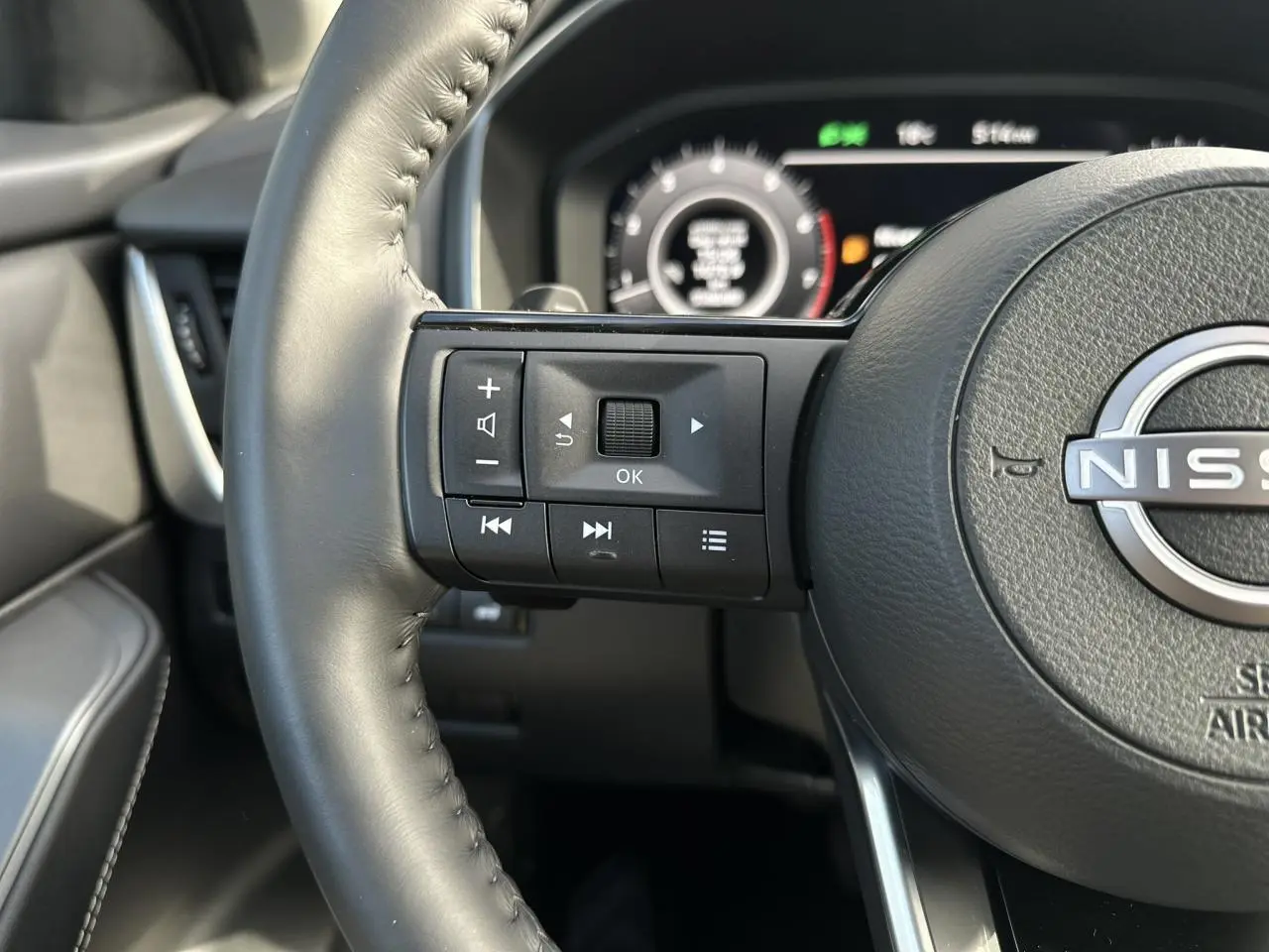Gros plan sur le volant cuir noir du Nissan Qashqai 2025 avec commandes audio et tableau de bord numérique en arrière-plan.