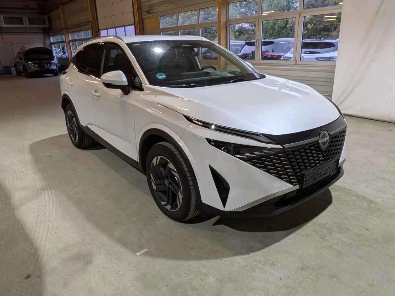 Nissan Qashqai blanc nacré en 3/4 avant droit, avec calandre noire distinctive et jantes alliage 18 pouces.