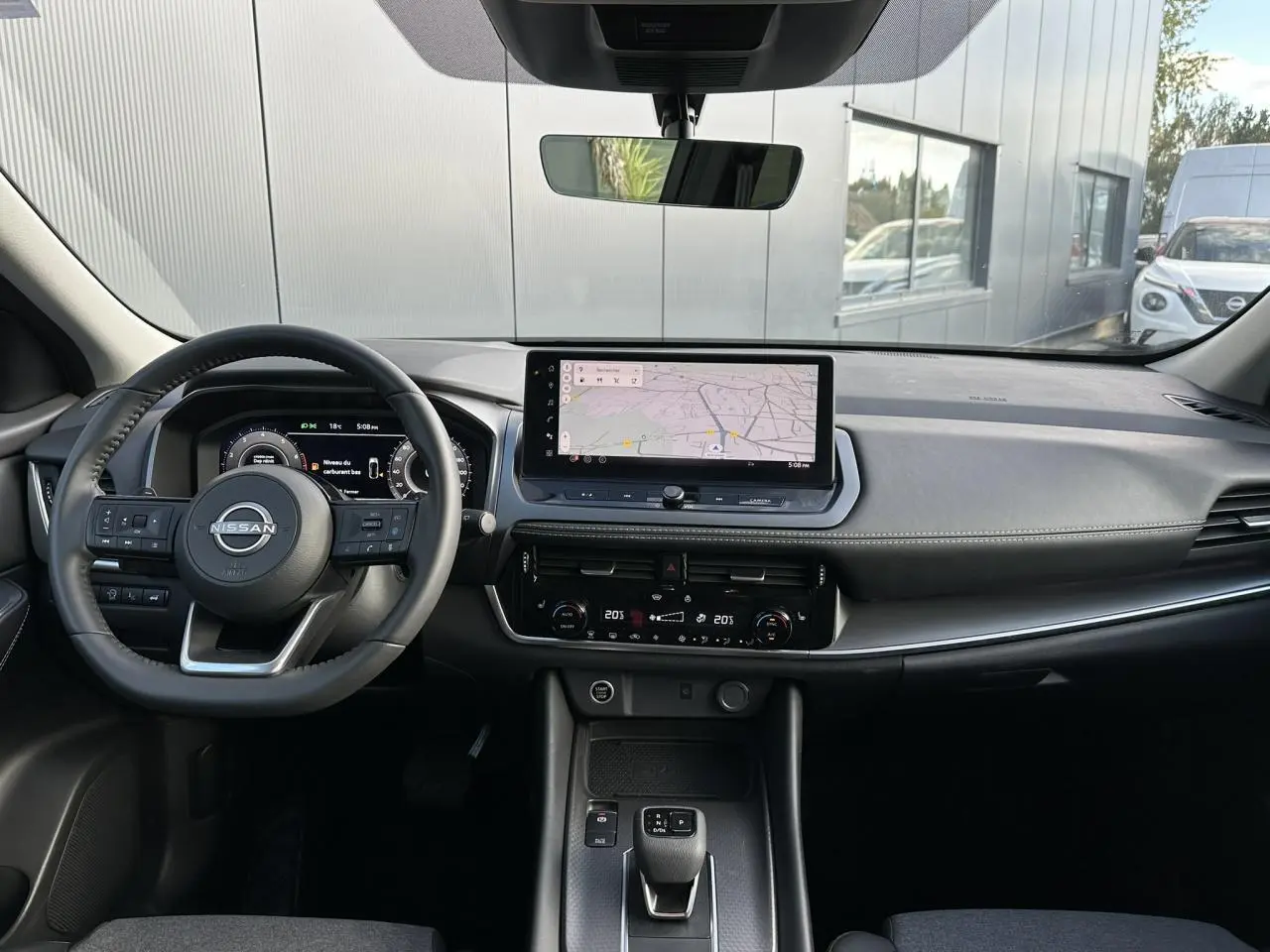 Vue intérieure frontale du tableau de bord du Nissan Qashqai blanc nacré 2025 avec écran tactile et volant cuir noir.