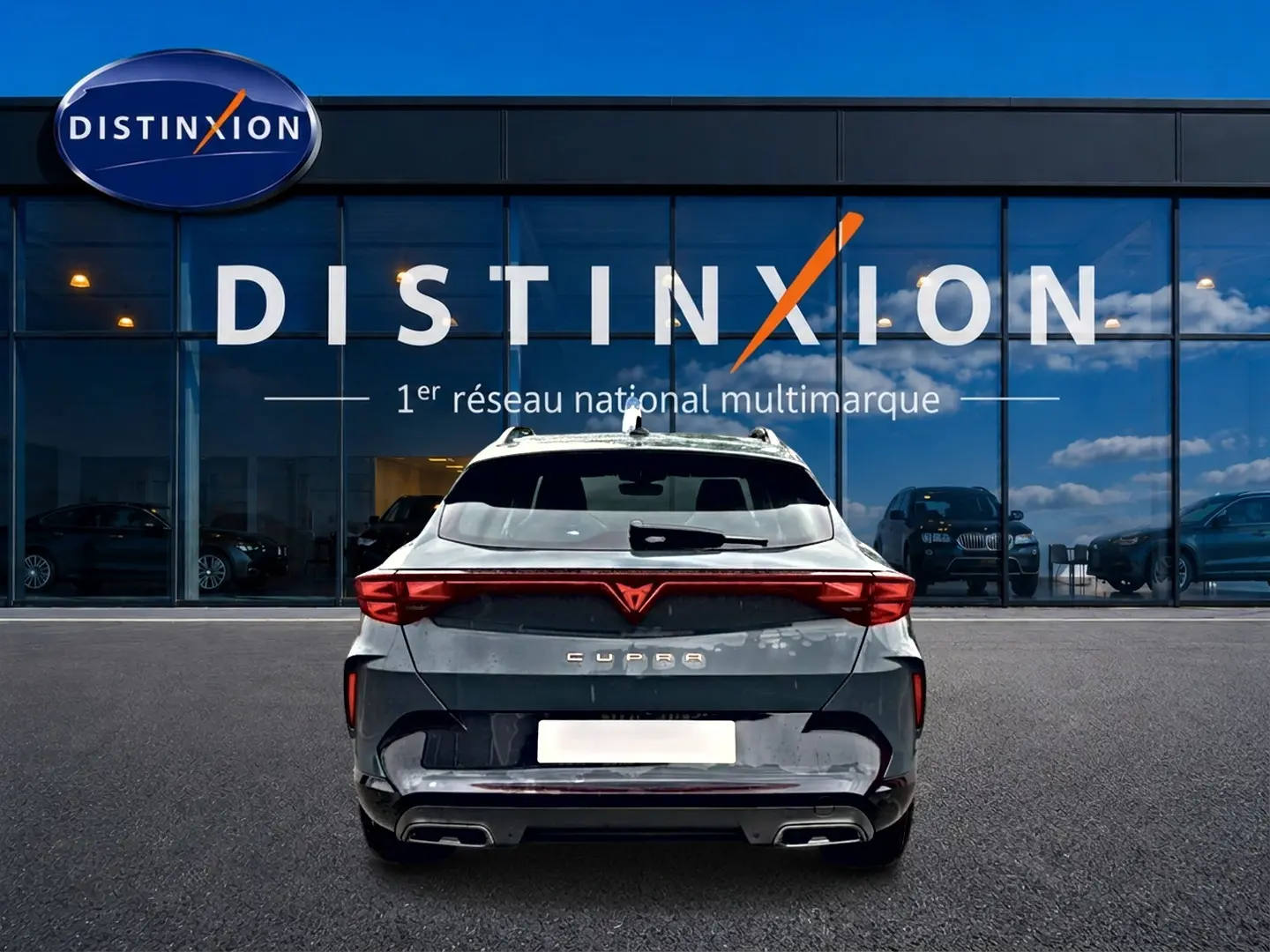 Vue arrière d'une CUPRA Formentor bleu fjord 2026 avec feux LED et double sortie d'échappement, devant un showroom Distinxion.