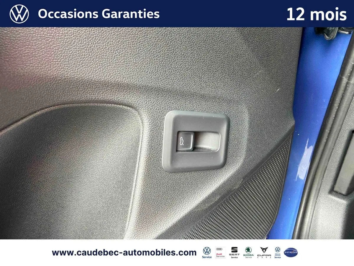 Détail du bouton d'ouverture du coffre sur la porte côté gauche d'un Volkswagen T-Roc bleu métallisé.