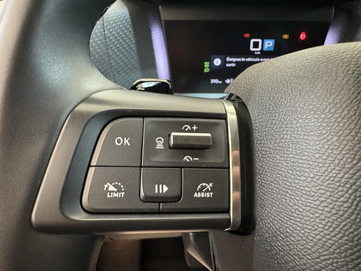 Gros plan sur les commandes au volant cuir noir de la Citroën C4 PureTech 130 EAT8 Shine 2023, avec affichage digital en arrière-plan.