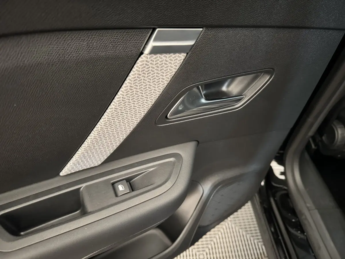 Gros plan sur la porte intérieure côté gauche noire avec poignée argentée et bouton de verrouillage fenêtre.