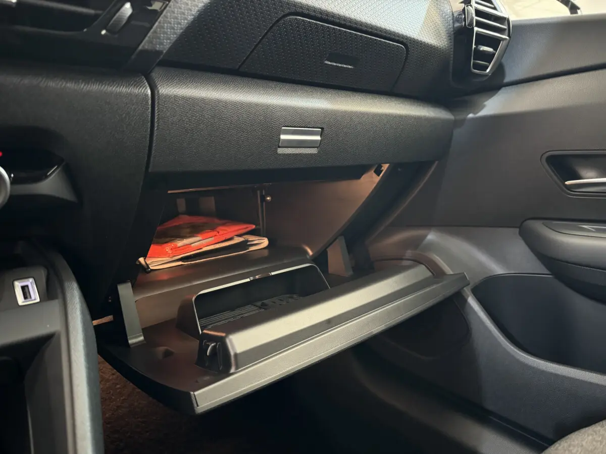 Vue intérieure côté passager du coffre à gants ouvert d'une Citroën C4 PureTech 130 EAT8 Shine noire, montrant des documents rouges.