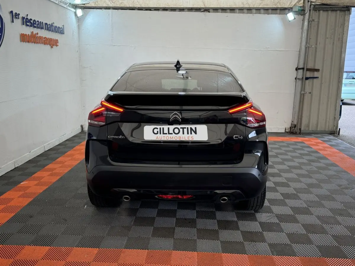 Vue arrière d'une Citroën C4 noire 2023 avec feux LED allumés dans un garage au sol damier noir et orange.