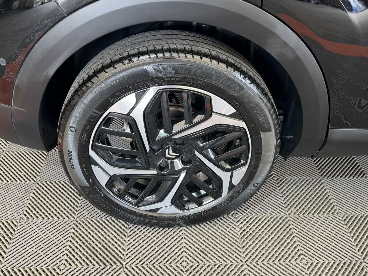 Gros plan sur la roue avant droite noire d'une Citroën C4 PureTech 130 EAT8 Shine avec jante alliage bicolore.