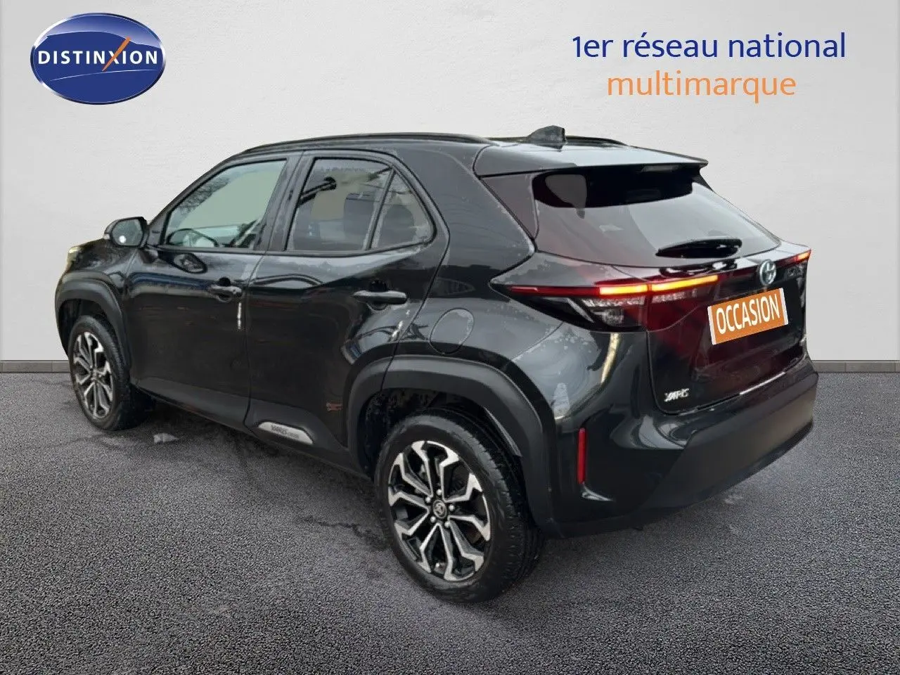 Toyota Yaris Cross 116h Design noir vue 3/4 arrière droit avec jantes bi-ton et feux arrière allumés.