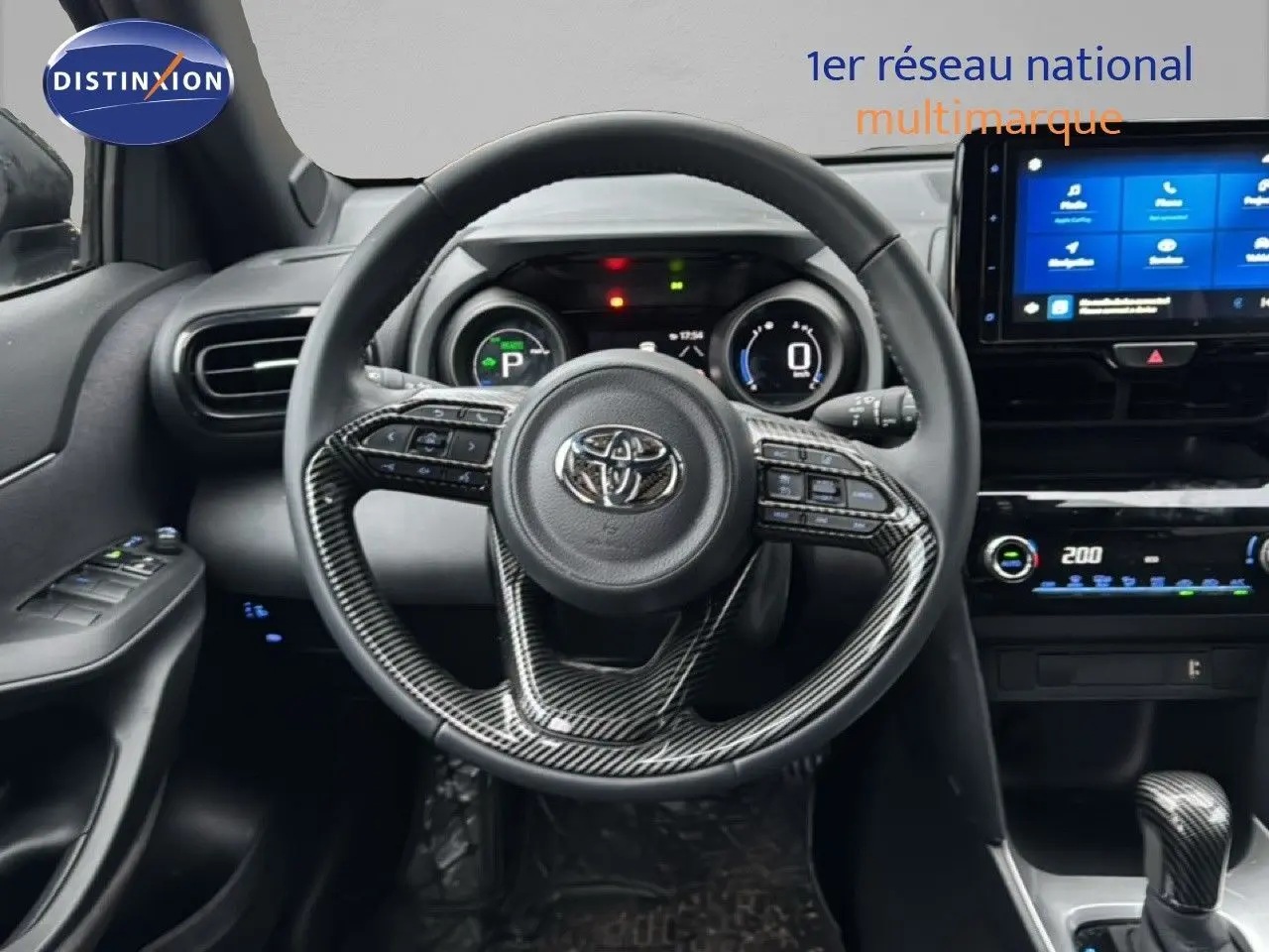 Vue intérieure du tableau de bord et volant en carbone d'une Toyota Yaris Cross 116h Design 2023 noire avec écran tactile et commandes intégrées.