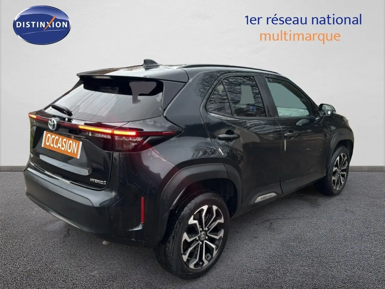 Vue 3/4 arrière droite d'une Toyota Yaris Cross 116h Design noire avec jantes bi-ton et feux arrière allumés.