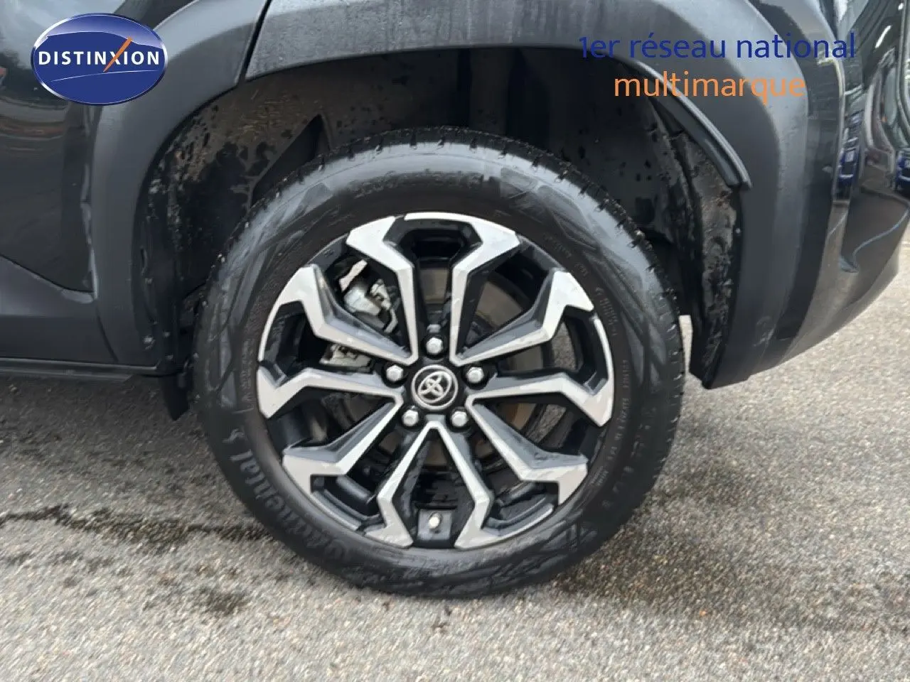 Gros plan sur la roue avant gauche noire d'une Toyota Yaris Cross 116h Design 2023 avec jante alliage bicolore.