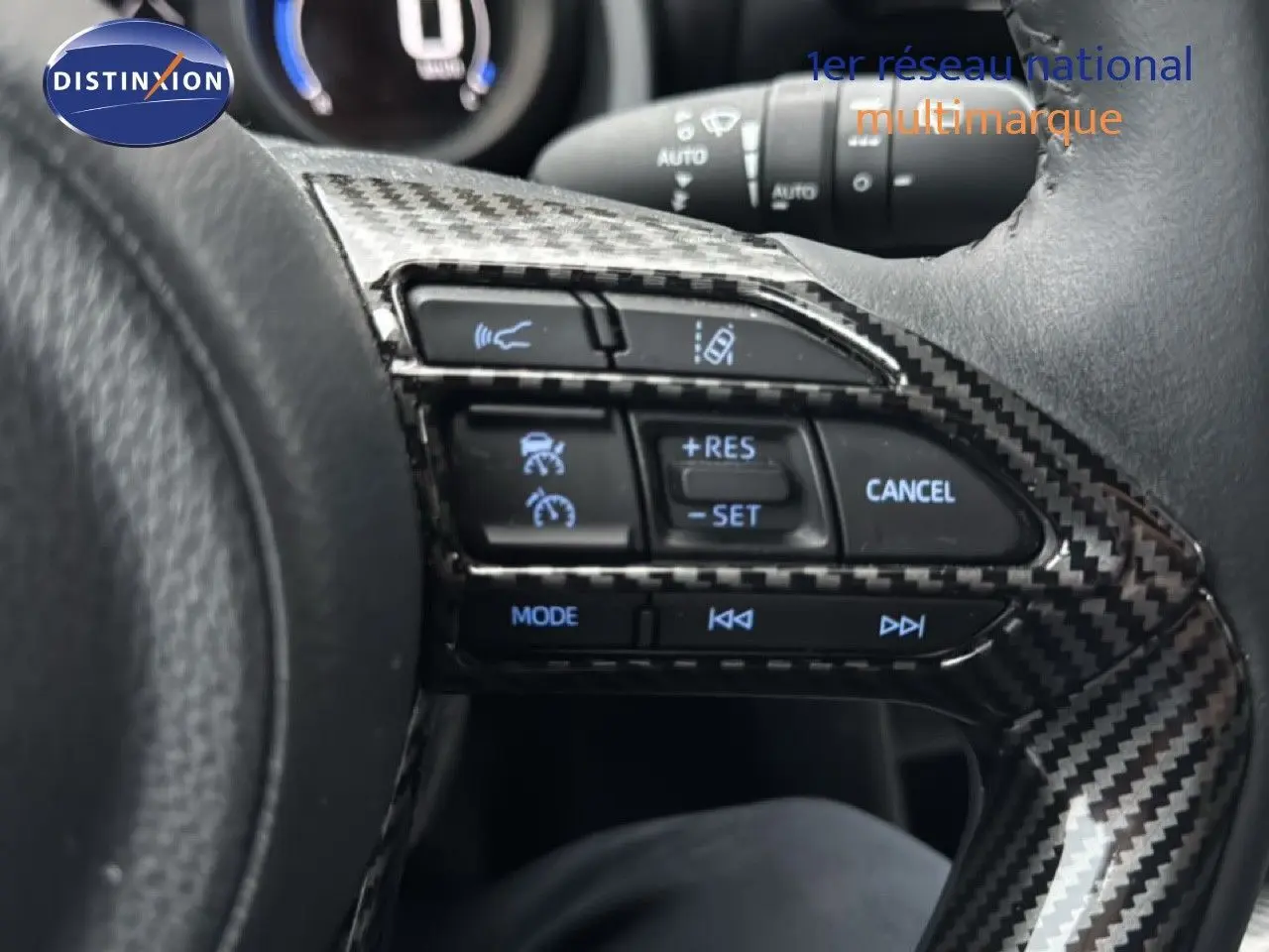 Gros plan sur les commandes au volant en carbone du Toyota Yaris Cross 116h Design noir, avec régulateur de vitesse et mode audio.
