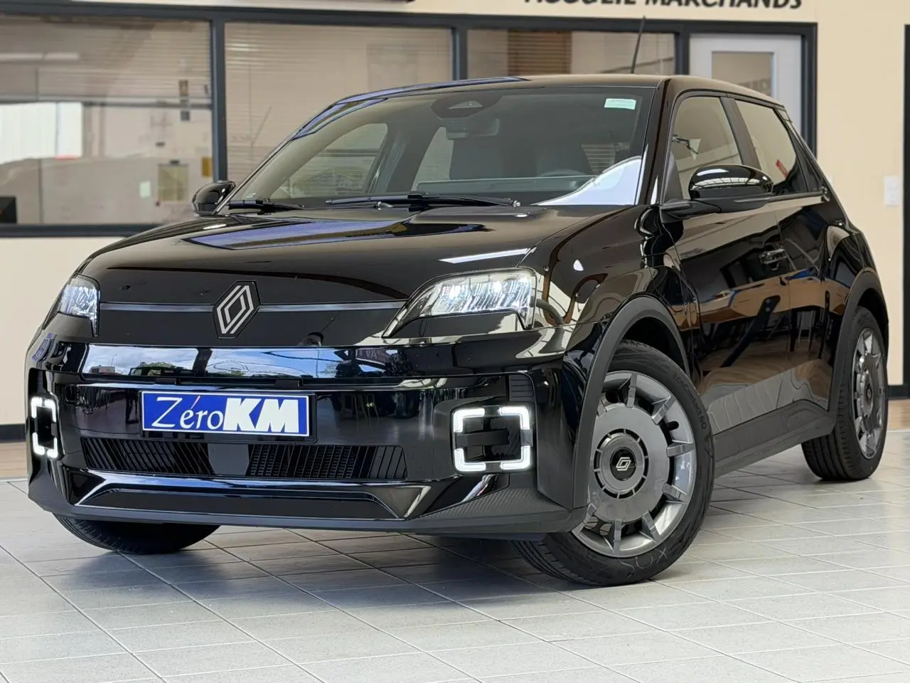 Renault R5 E-Tech électrique noir étoilé vue 3/4 avant avec phares et feux LED distinctifs en intérieur showroom.