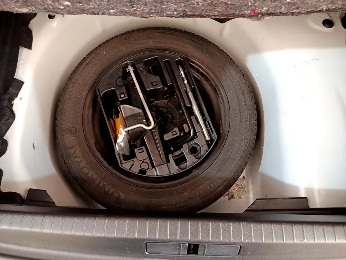 Vue plongeante sur la roue de secours noire et les outils dans le coffre blanc d'une Peugeot 208 blanche.