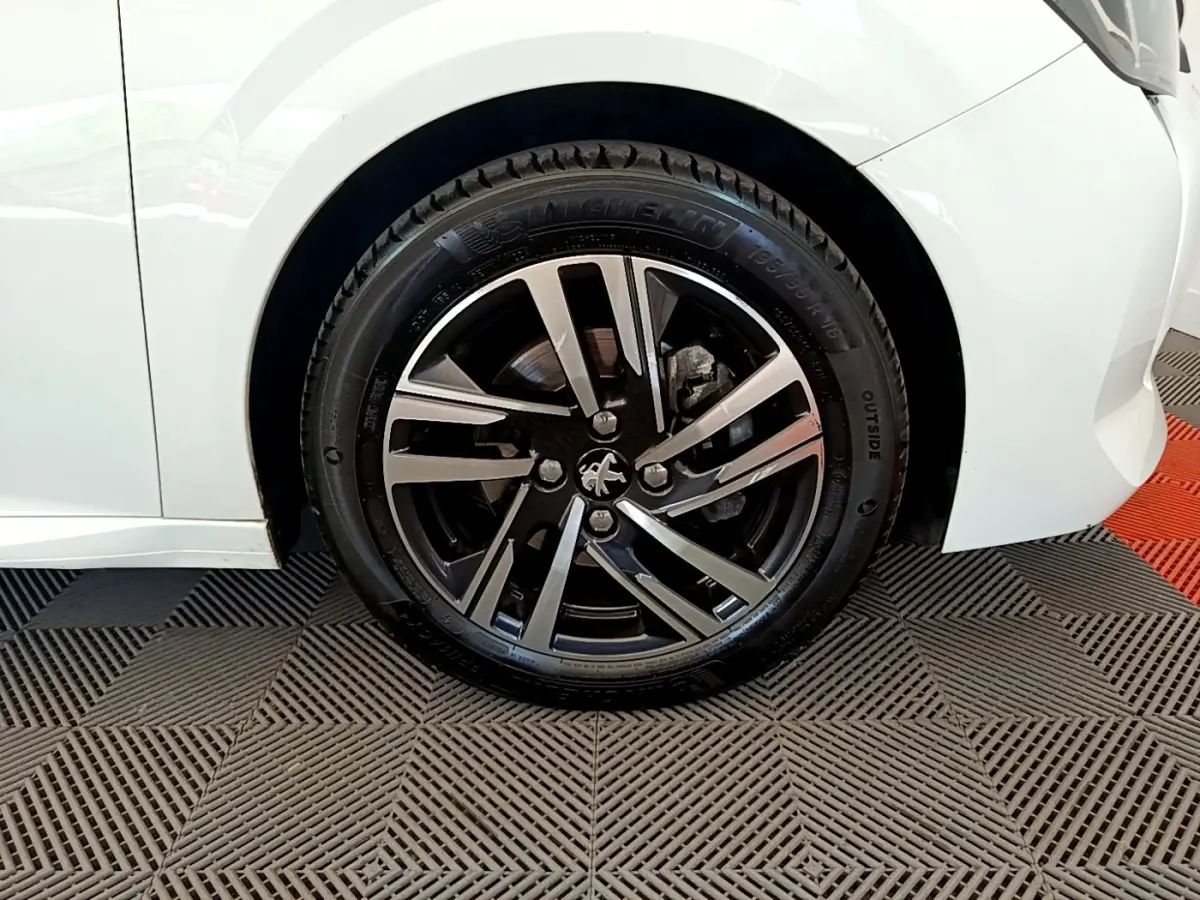 Gros plan sur la roue avant droite d’une Peugeot 208 blanche, mettant en valeur la jante alliage noire et argent.