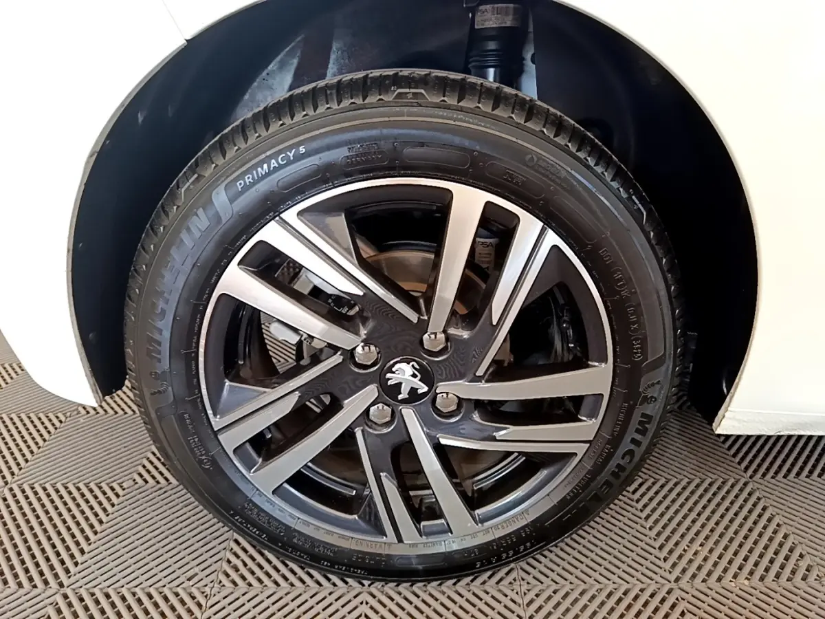 Gros plan sur la roue avant droite d'une Peugeot 208 blanche, mettant en valeur la jante alliage bicolore et le pneu Michelin.