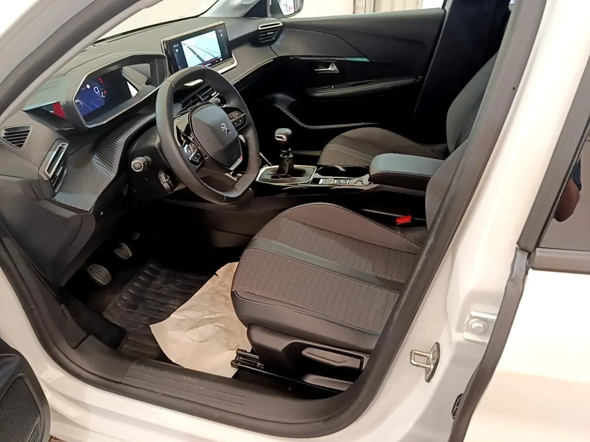 Intérieur avant droit d’une Peugeot 208 blanche, avec tableau de bord numérique et écran tactile central visible.