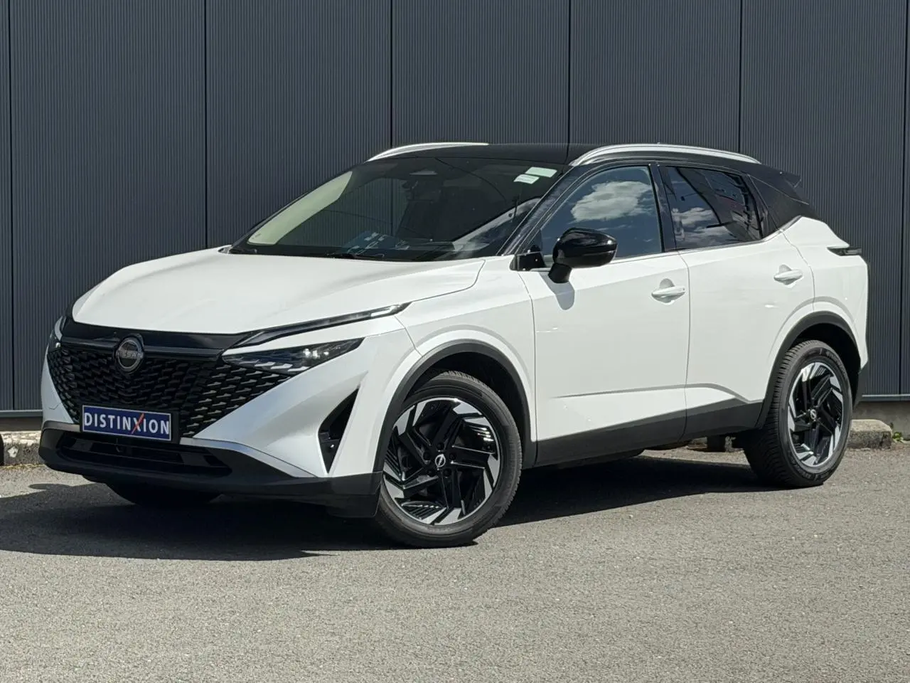 Nissan Qashqai blanc nacré avec toit noir, vu en 3/4 avant droit, jantes alliage noires et calandre distinctive.