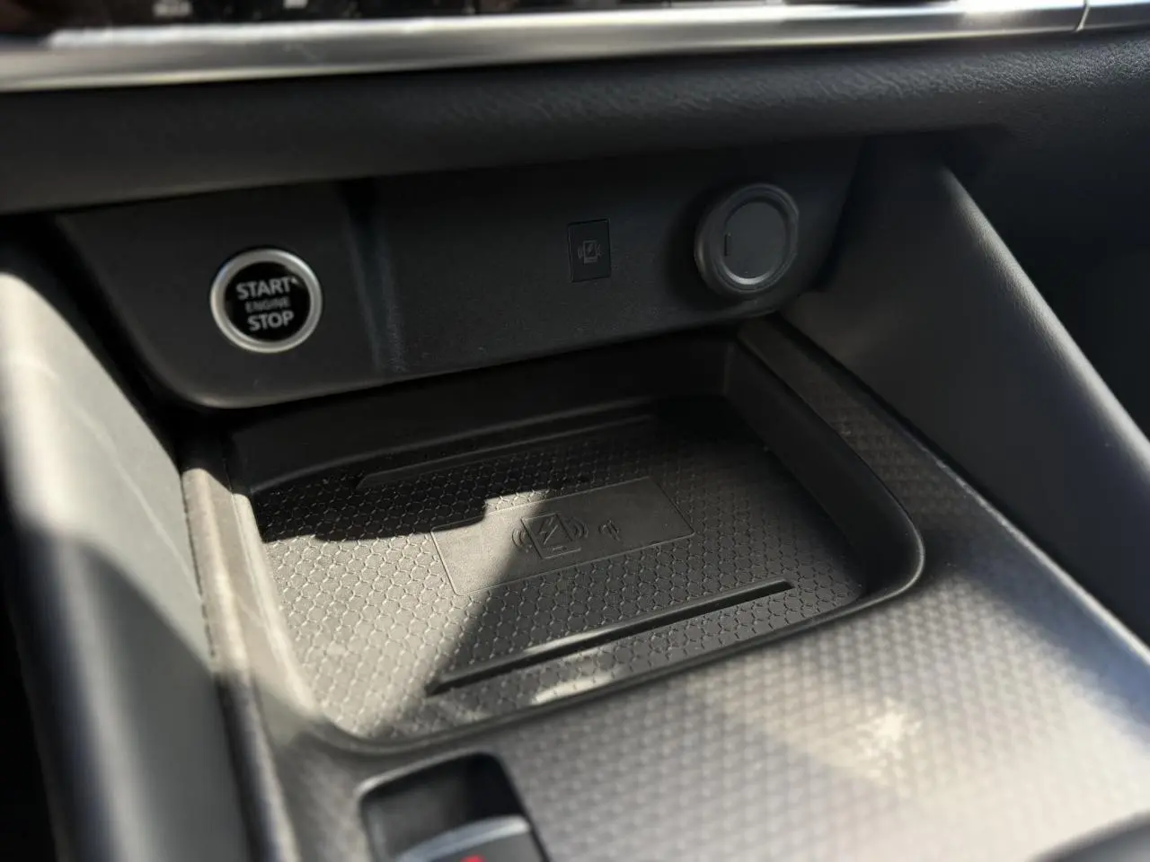 Gros plan sur la console centrale noire du Nissan Qashqai 2025, avec zone de charge sans fil et bouton Start/Stop.