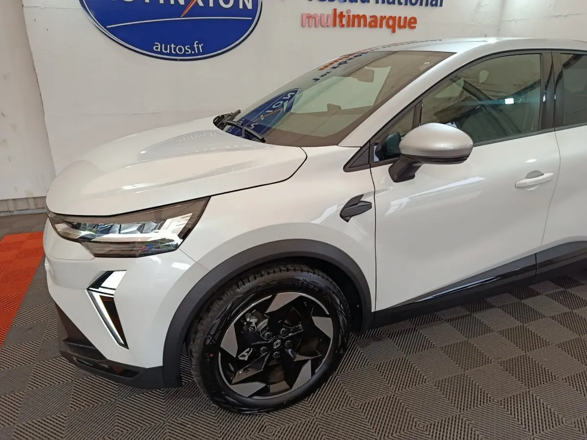 Vue 3/4 avant droit du Renault Captur blanc avec jantes noires et détails de phares LED modernes.
