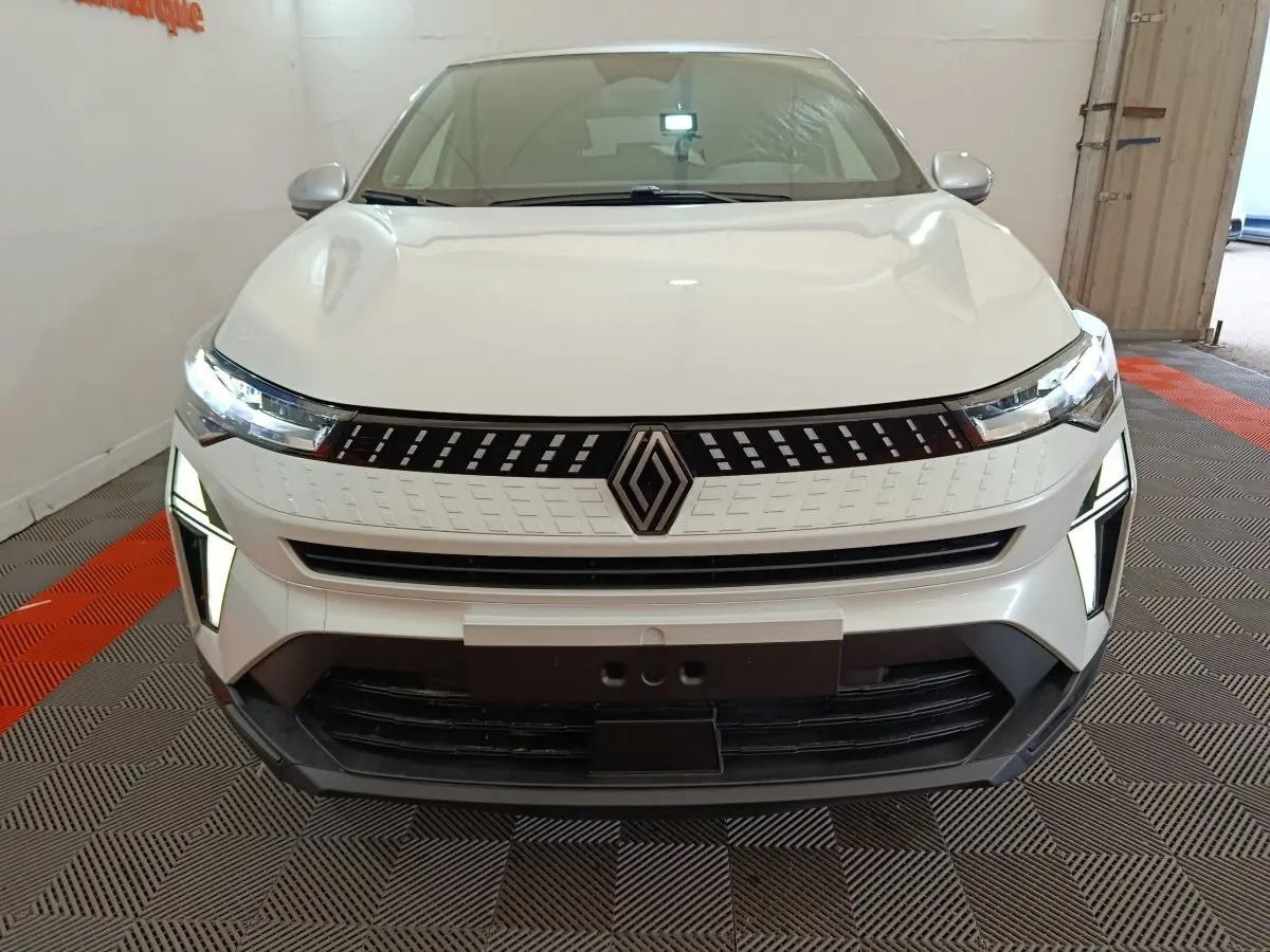 Vue de face du Renault Captur blanc 2025 avec phares LED allumés et calandre moderne en intérieur showroom.