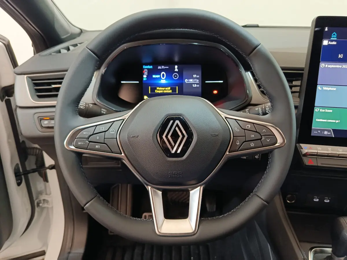 Vue rapprochée du volant en cuir noir du Renault Captur blanc 2025 avec tableau de bord numérique et écran tactile central.