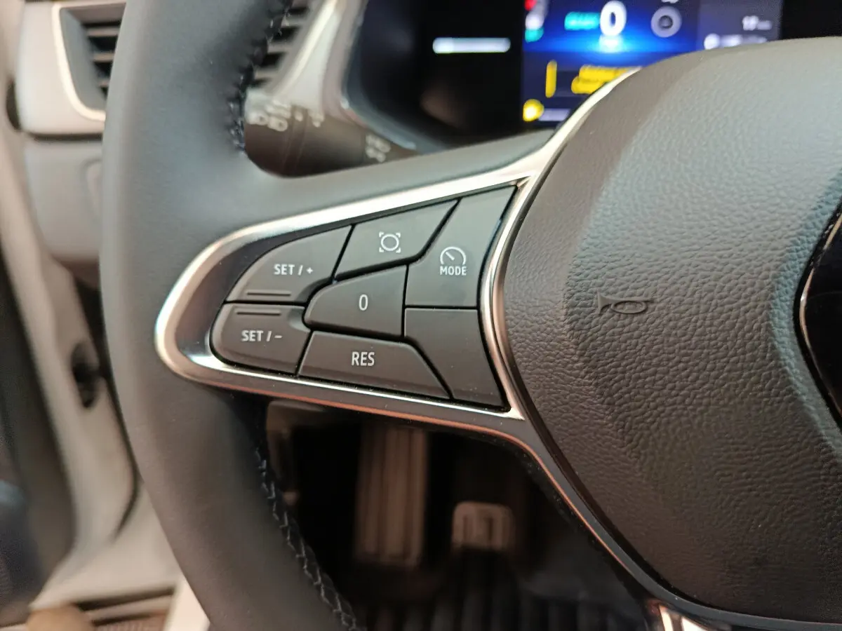 Gros plan sur les commandes au volant côté gauche du Renault Captur blanc techno E-Tech 2025 avec affichage numérique en arrière-plan.