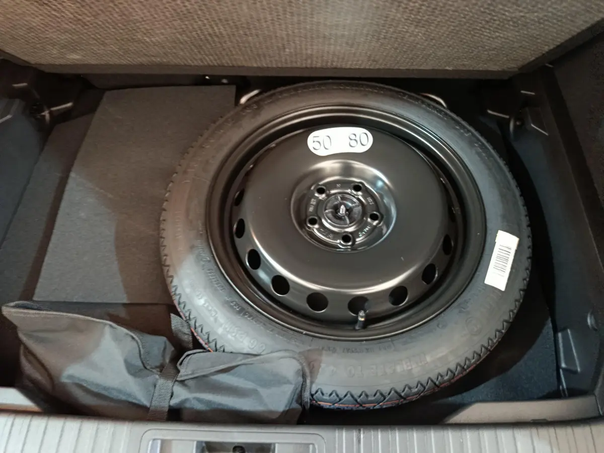 Roue de secours noire dans le coffre du Renault Captur blanc 2025, vue plongeante sur le pneu compact.