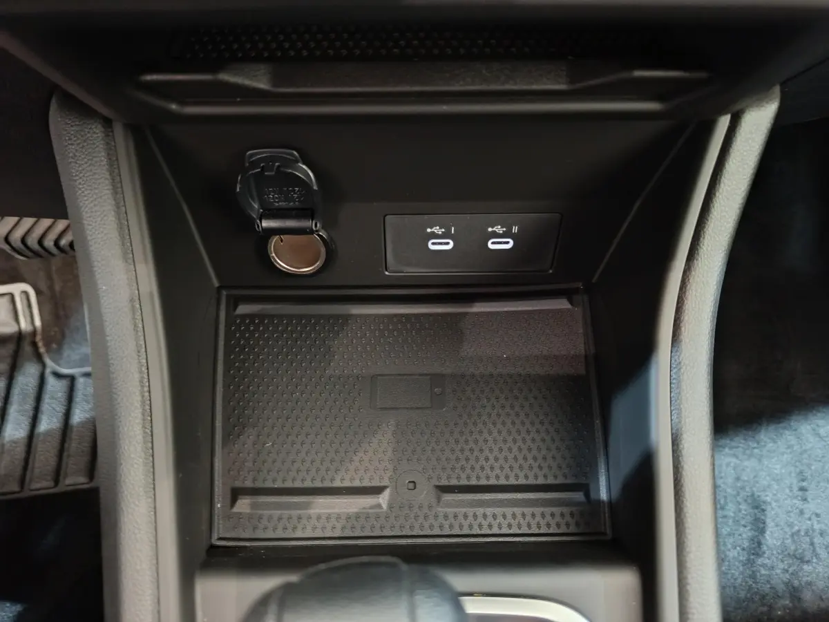 Gros plan sur la console centrale du Renault Captur blanc 2025, montrant prises USB et prise 12V dans un espace de rangement noir.