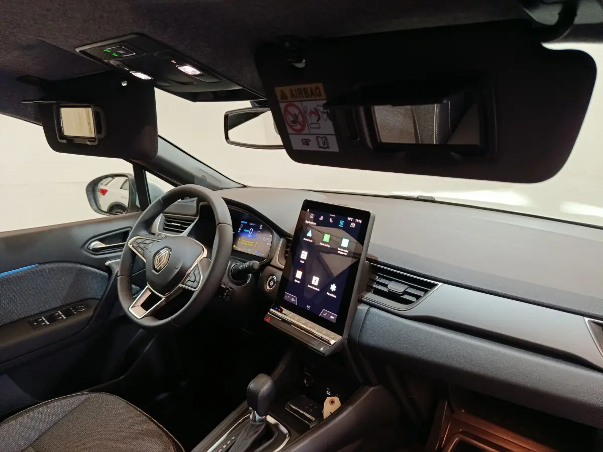 Vue intérieure côté conducteur du tableau de bord du Renault Captur blanc 2025 avec écran tactile vertical et volant multifonctions.