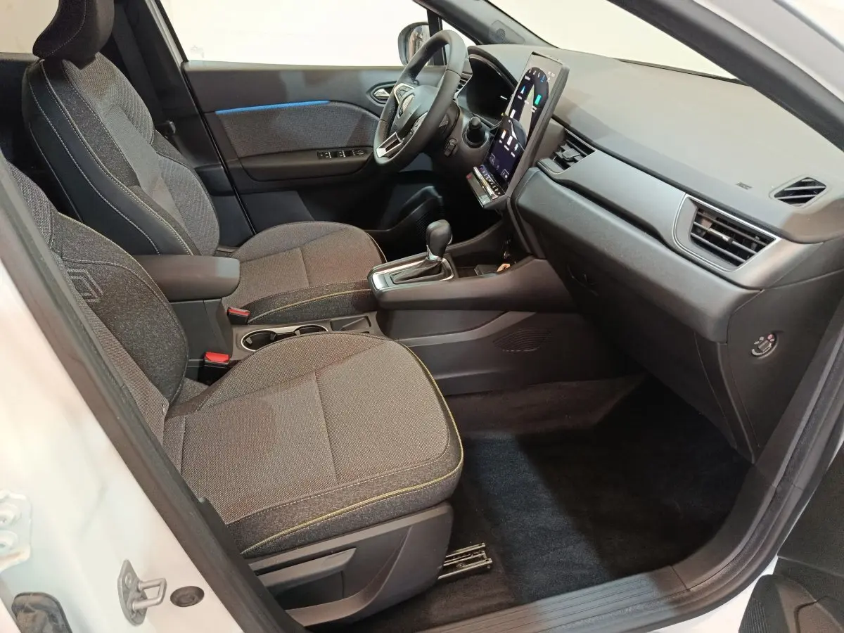 Intérieur avant droit du Renault Captur blanc 2025, sièges gris, écran tactile vertical et volant multifonctions.