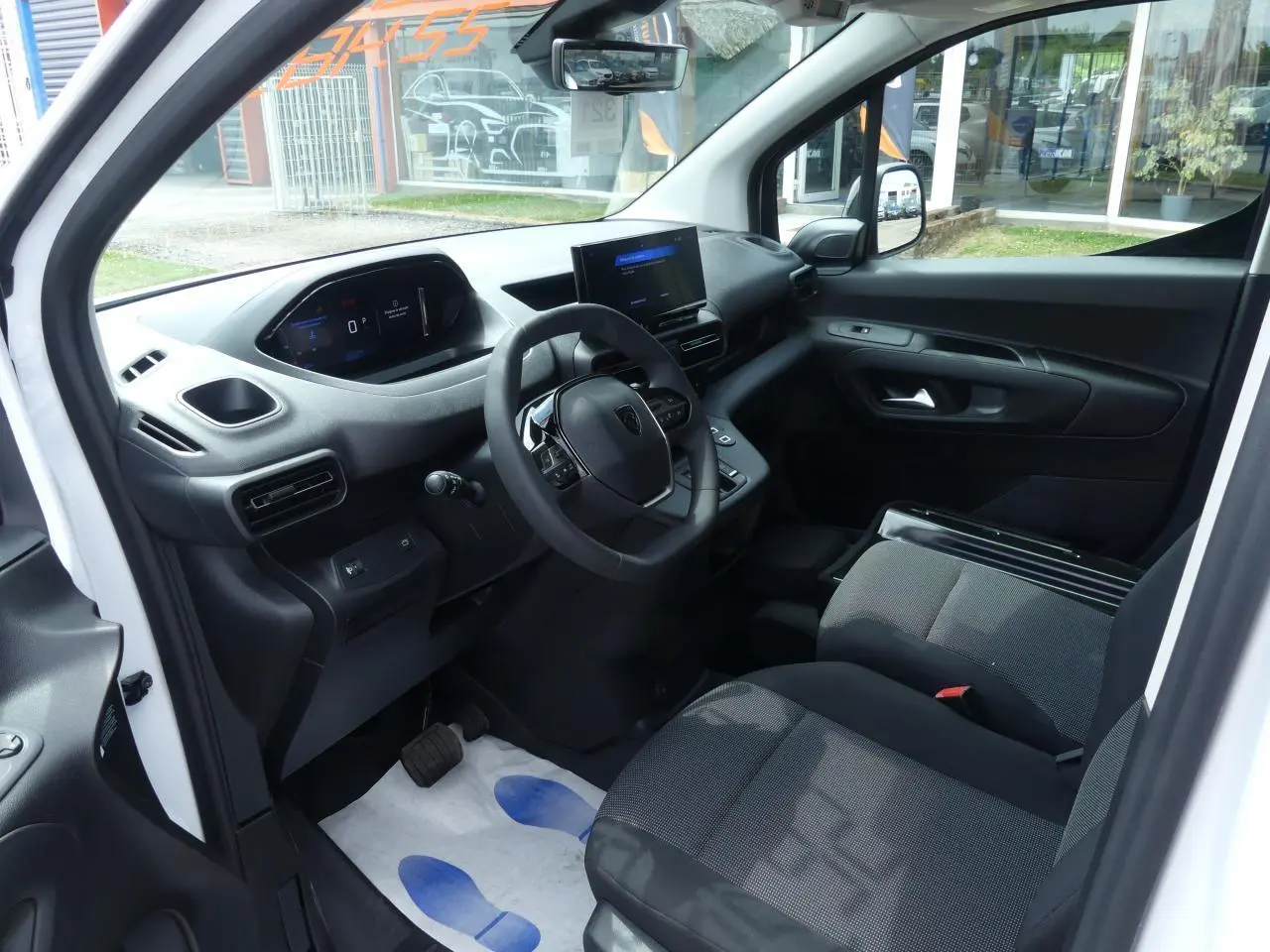Vue intérieure côté conducteur du Peugeot Partner blanc 2025, avec tableau de bord numérique et écran tactile central.