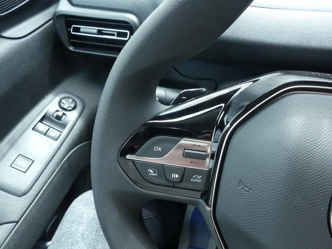 Gros plan sur les commandes gauche du volant noir du Peugeot Partner blanc, avec bouton OK et régulateur de vitesse.