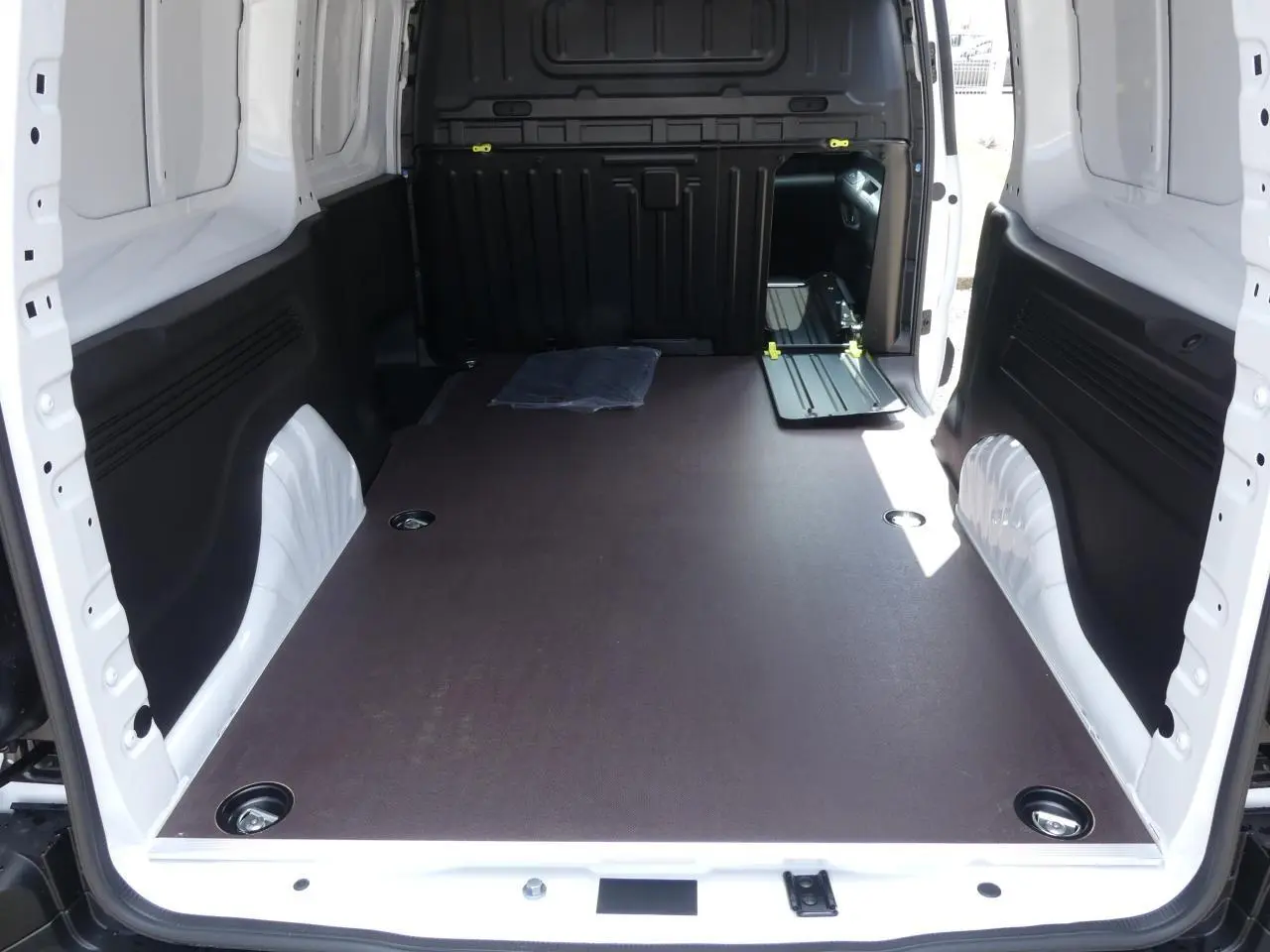 Vue intérieure arrière du Peugeot Partner XL blanc, montrant l'espace de chargement avec plancher bois antidérapant et parois blanches.