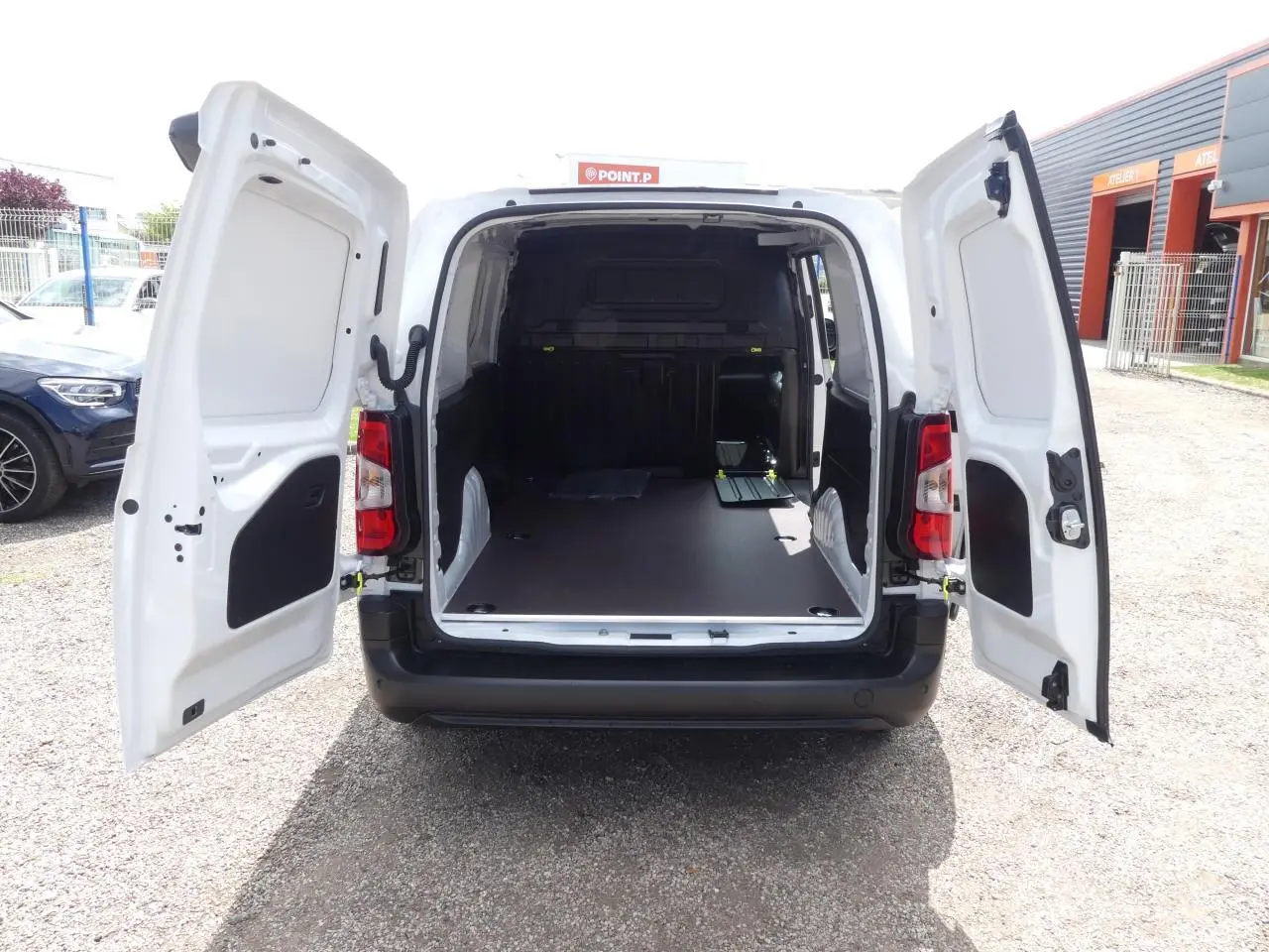 Vue arrière du Peugeot Partner blanc 2025 avec portes ouvertes montrant l'espace de chargement vide et plancher bois antidérapant.