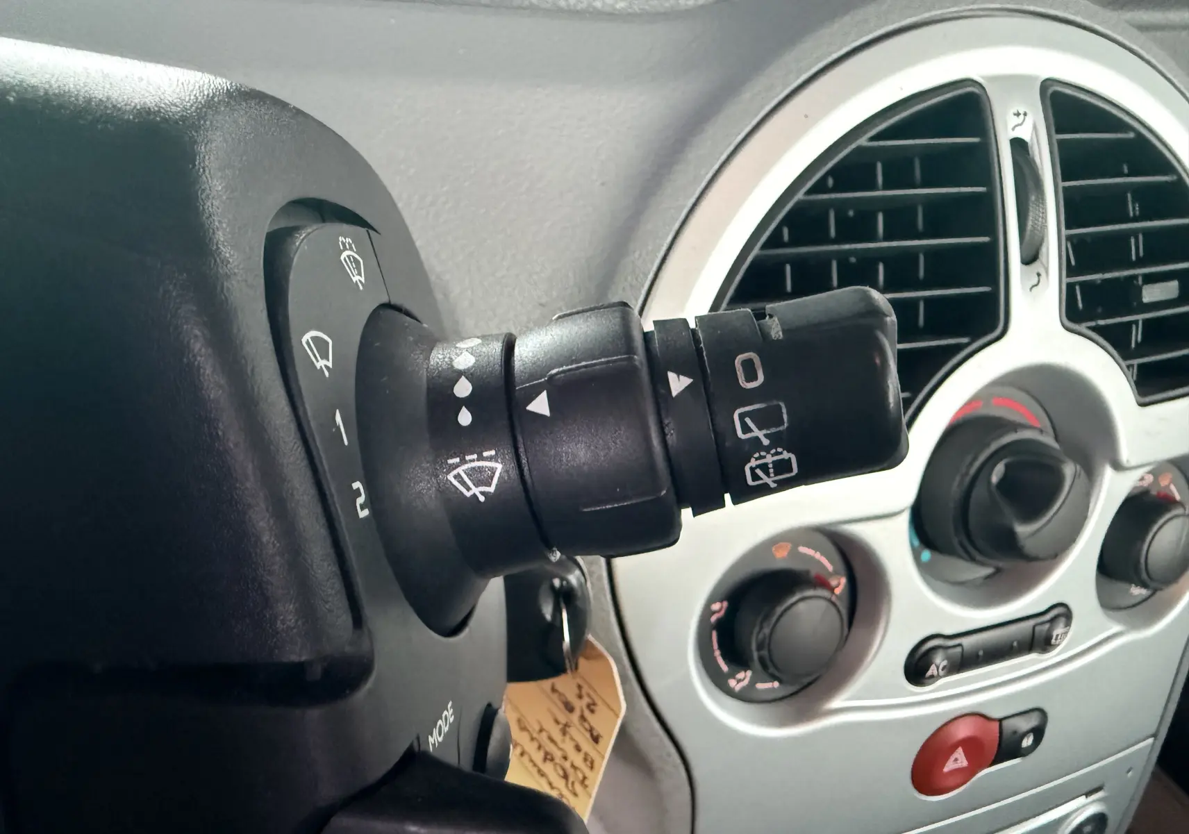 Gros plan sur la commande d’essuie-glace à gauche du volant dans l’habitacle gris d’une Renault Modus beige de 2011.
