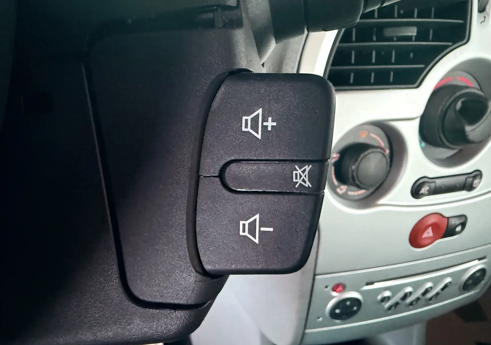 Gros plan sur les commandes de volume audio au volant d’une Renault Modus beige, tableau de bord gris en arrière-plan.