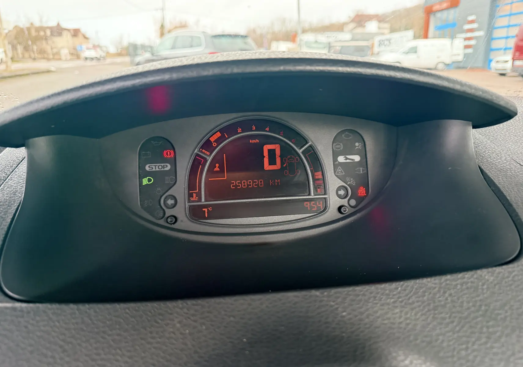 Vue rapprochée du tableau de bord numérique de la Renault Modus beige, affichant 258328 km et 7°C.