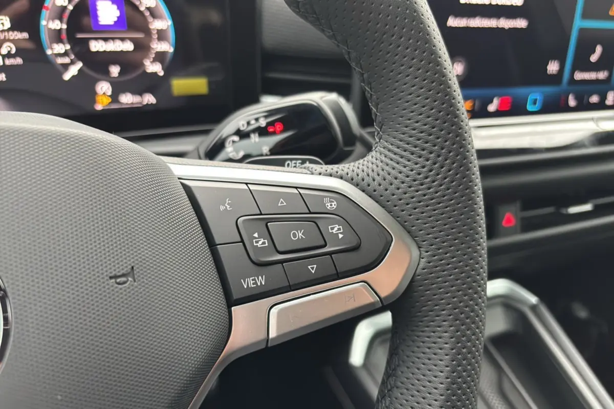 Gros plan sur le volant cuir perforé du Volkswagen T-Roc 2026 avec commandes multifonctions et affichage digital en arrière-plan.