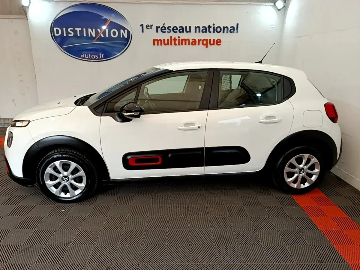 Vue de profil côté gauche d'une Citroën C3 blanche avec inserts noirs et rouge sur les portes, en intérieur showroom.