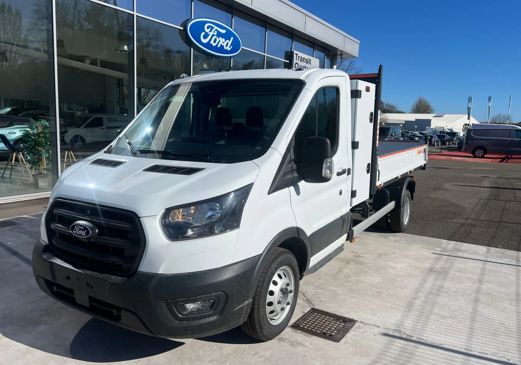Ford Transit Chassis Cabine blanc en 3/4 avant droit, avec benne et coffre visibles sur parking extérieur.