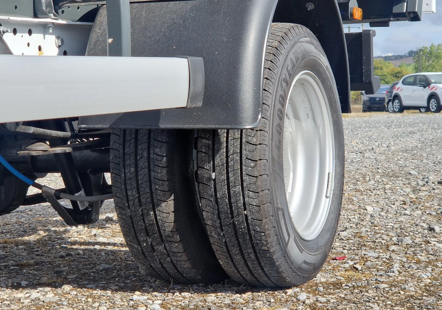 Gros plan sur les roues jumelées arrière du Ford Transit Châssis Cabine blanc, avec benne et coffre visibles partiellement.