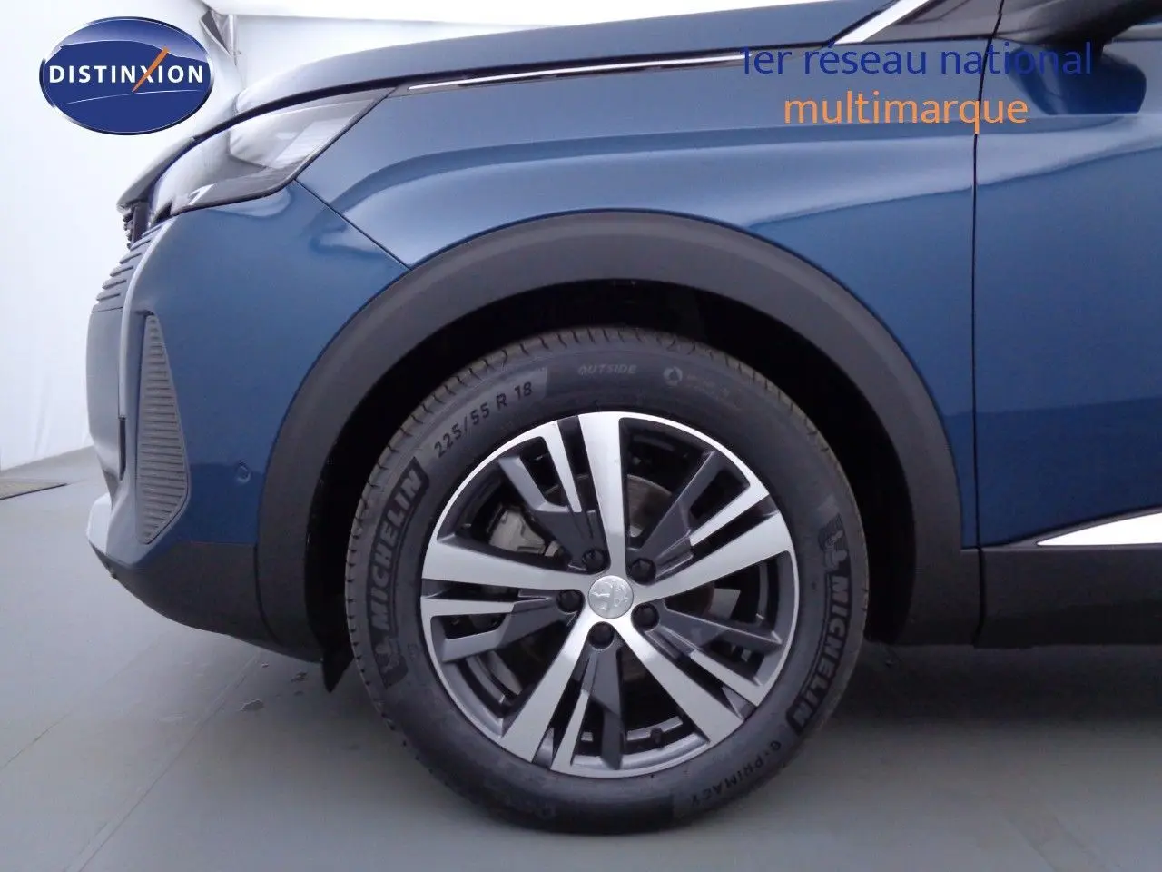 Gros plan sur la roue avant gauche d'un Peugeot 3008 2023 bleu Célèbes Métal avec jante alliage bicolore.