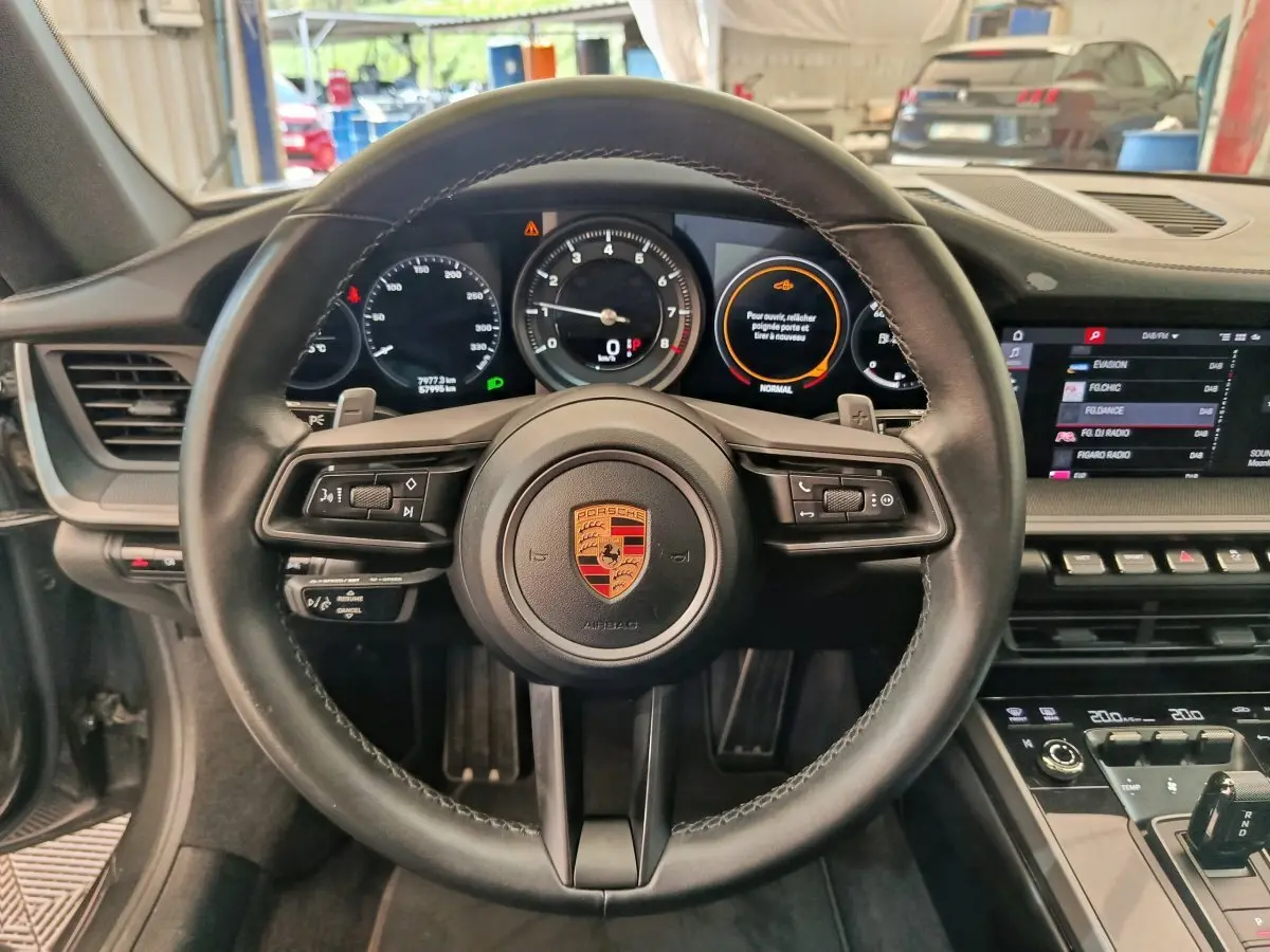 Vue intérieure centrée sur le volant cuir de la Porsche 911 Carrera 4S 2019 avec tableau de bord digital et écran tactile.