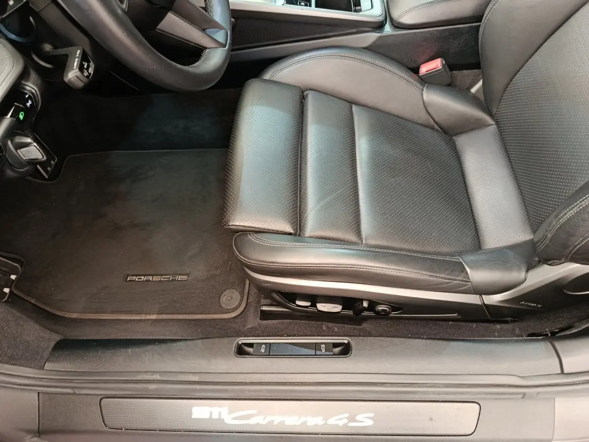 Vue rapprochée du siège conducteur en cuir noir et tapis de sol Porsche d'une 911 Carrera 4S Coupé gris foncé.