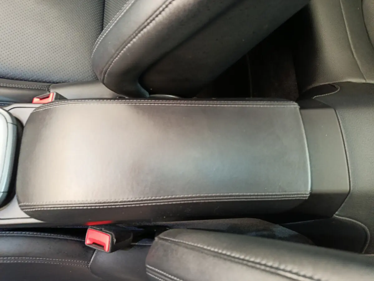 Vue rapprochée de l'accoudoir central en cuir noir et des ceintures de sécurité rouges dans l'habitacle d'une Porsche 911 Carrera 4S Coupé 2019.